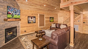 L’intérieur d’un chalet confortable, avec une cheminée, un canapé en cuir, des murs en bois et un téléviseur fixé au mur.