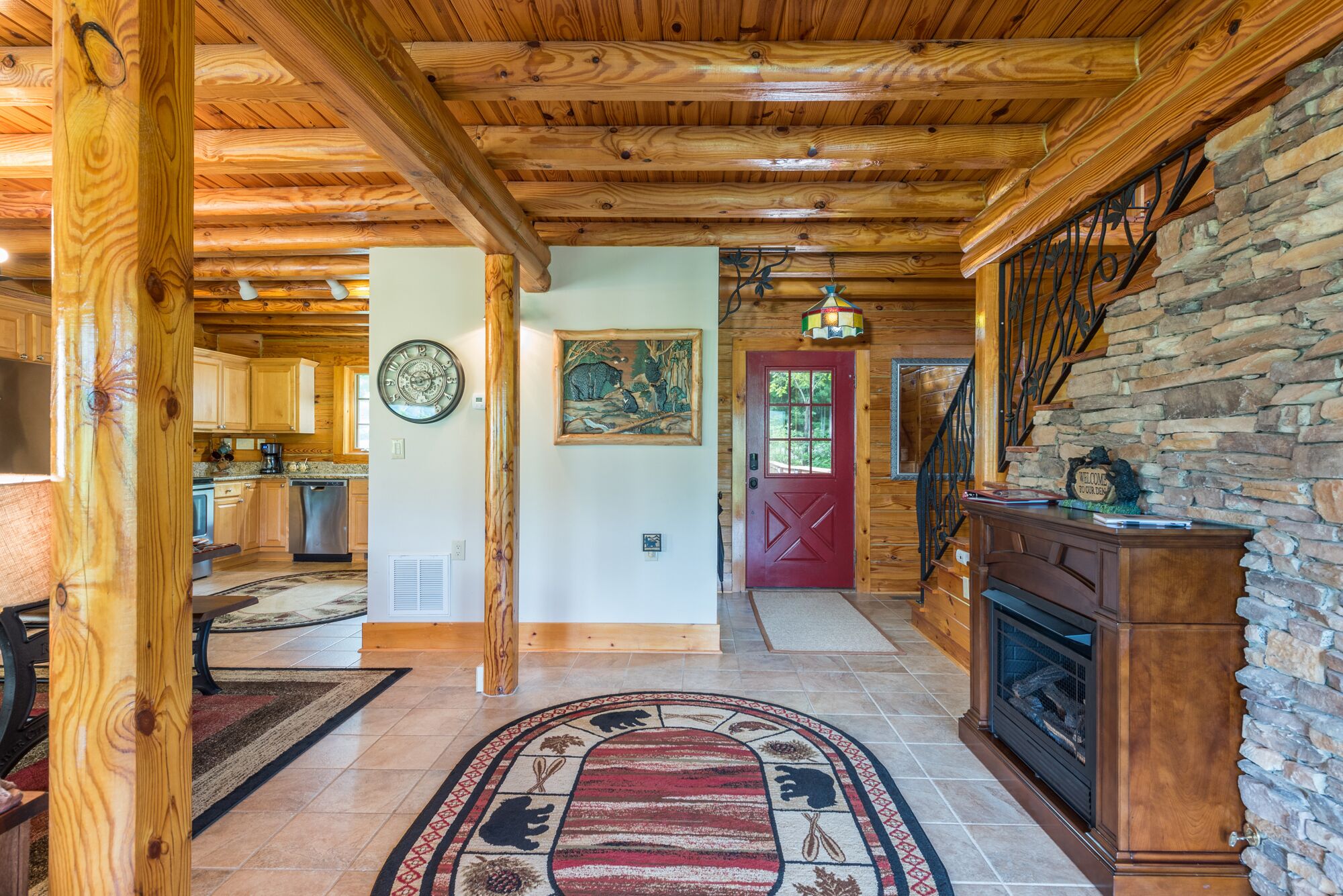 Un intérieur en bois avec une cheminée en pierre, une porte rouge et un coin cuisine visible au fond.