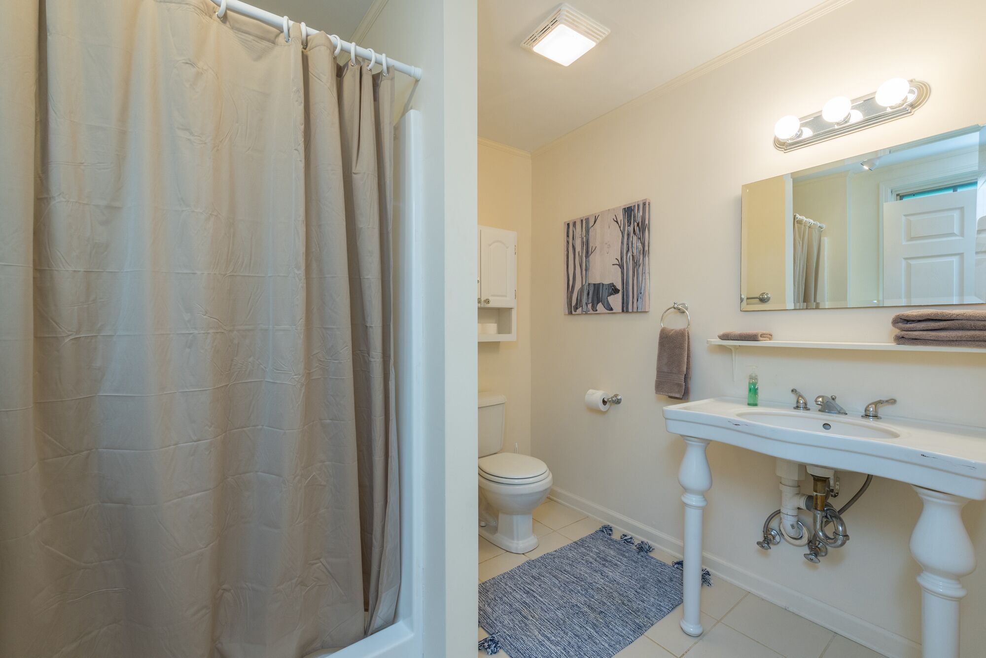 A bathroom with a shower curtain, toilet, sink, and a mirror with lights above.