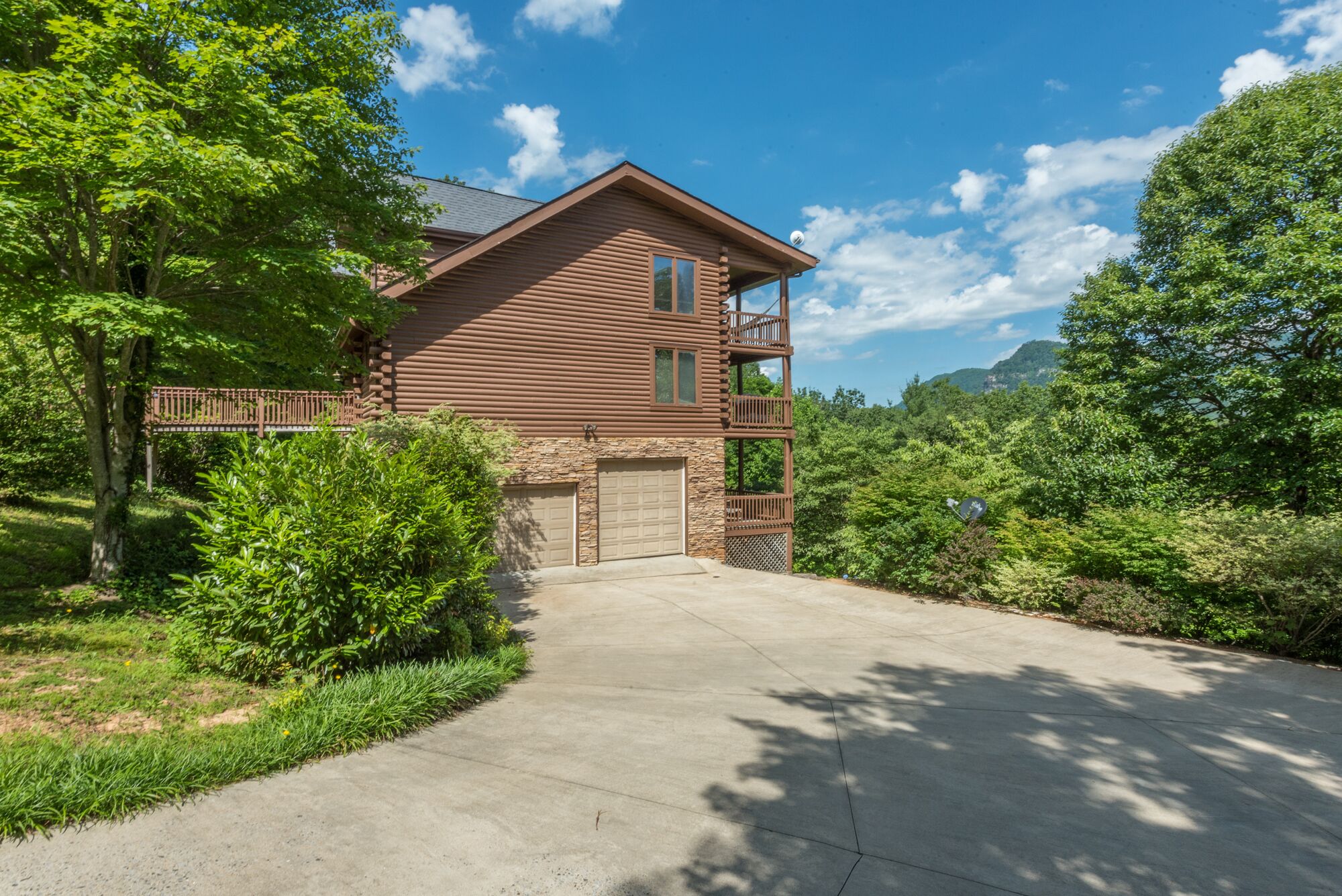 A two-story log cabin with a stone foundation, a garage, and a balcony.