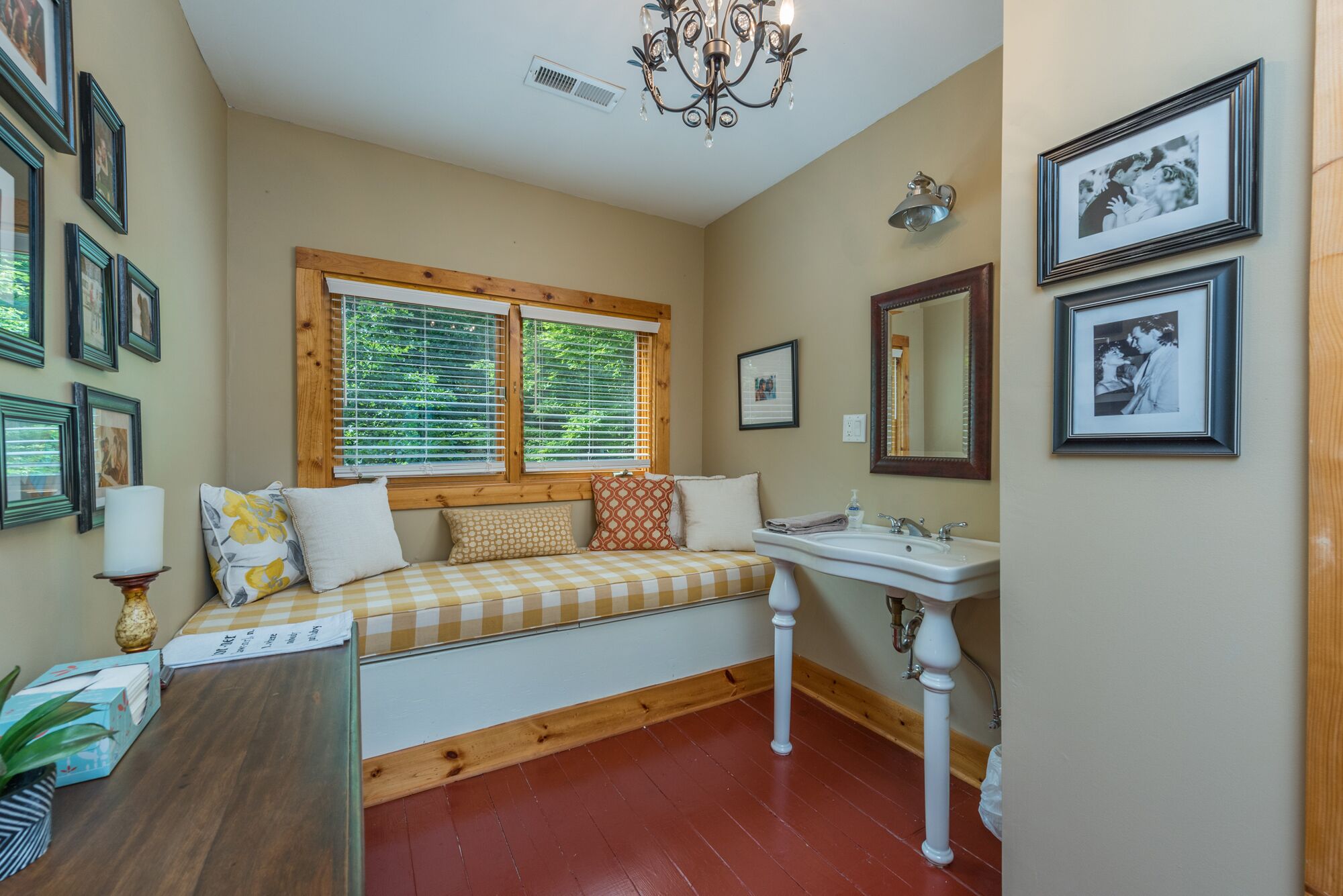 A cozy room with a checkered bench, a wooden window frame, a white sink, and framed pictures on the walls.