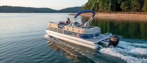 A motorboat on a calm lake with a canopy, surrounded by trees and hills in the background.