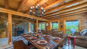 L’intérieur d’un chalet en bois comprend une table à manger pour quatre personnes, une cheminée et un mur en pierre.