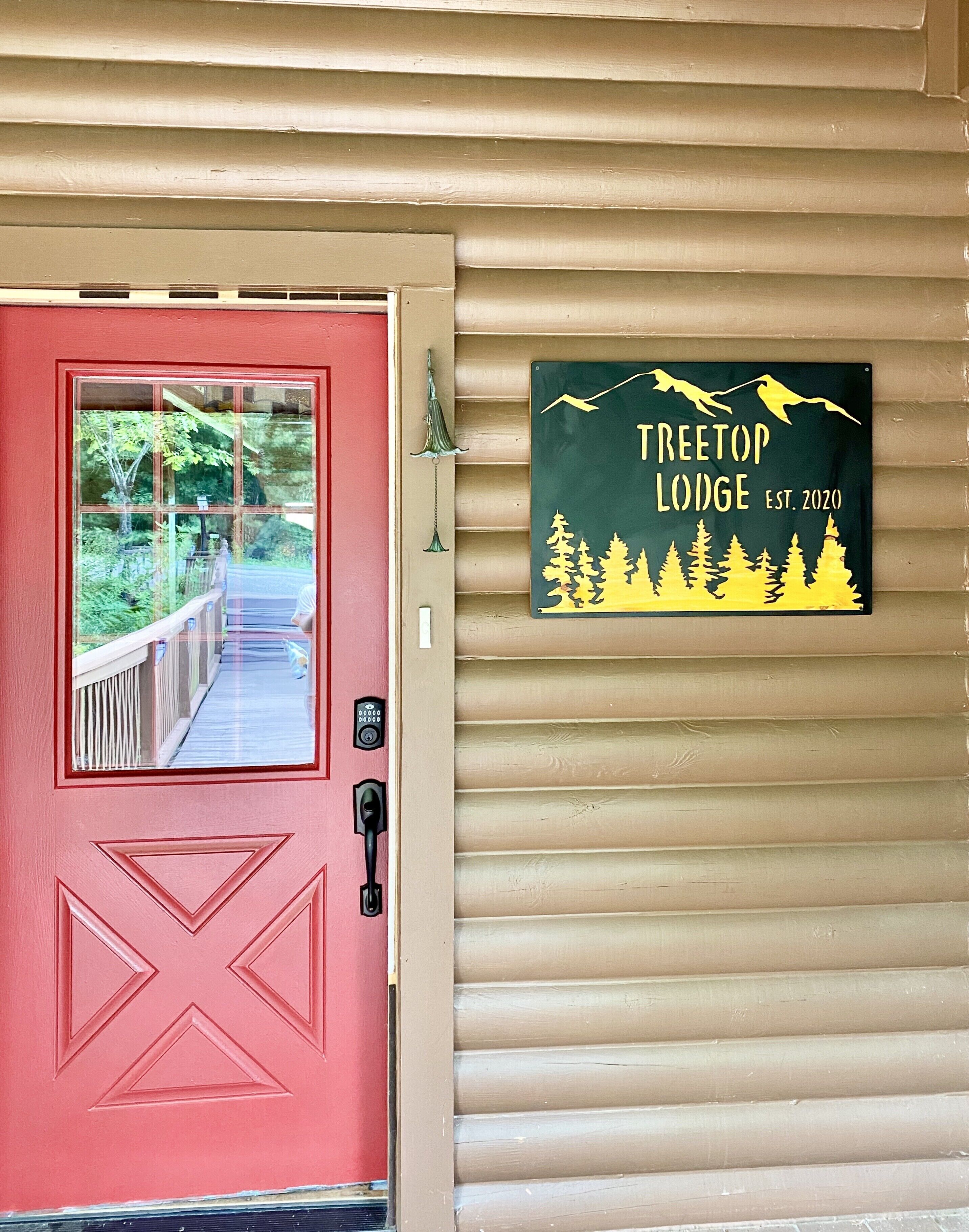 A red door with a window, a doorbell, and a sign for Treetop Lodge.
