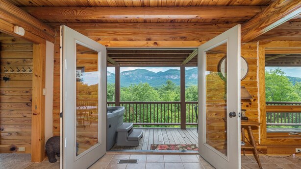 Une porte en bois ouverte donnant sur un balcon équipé d’un jacuzzi et offrant une vue sur les montagnes.
