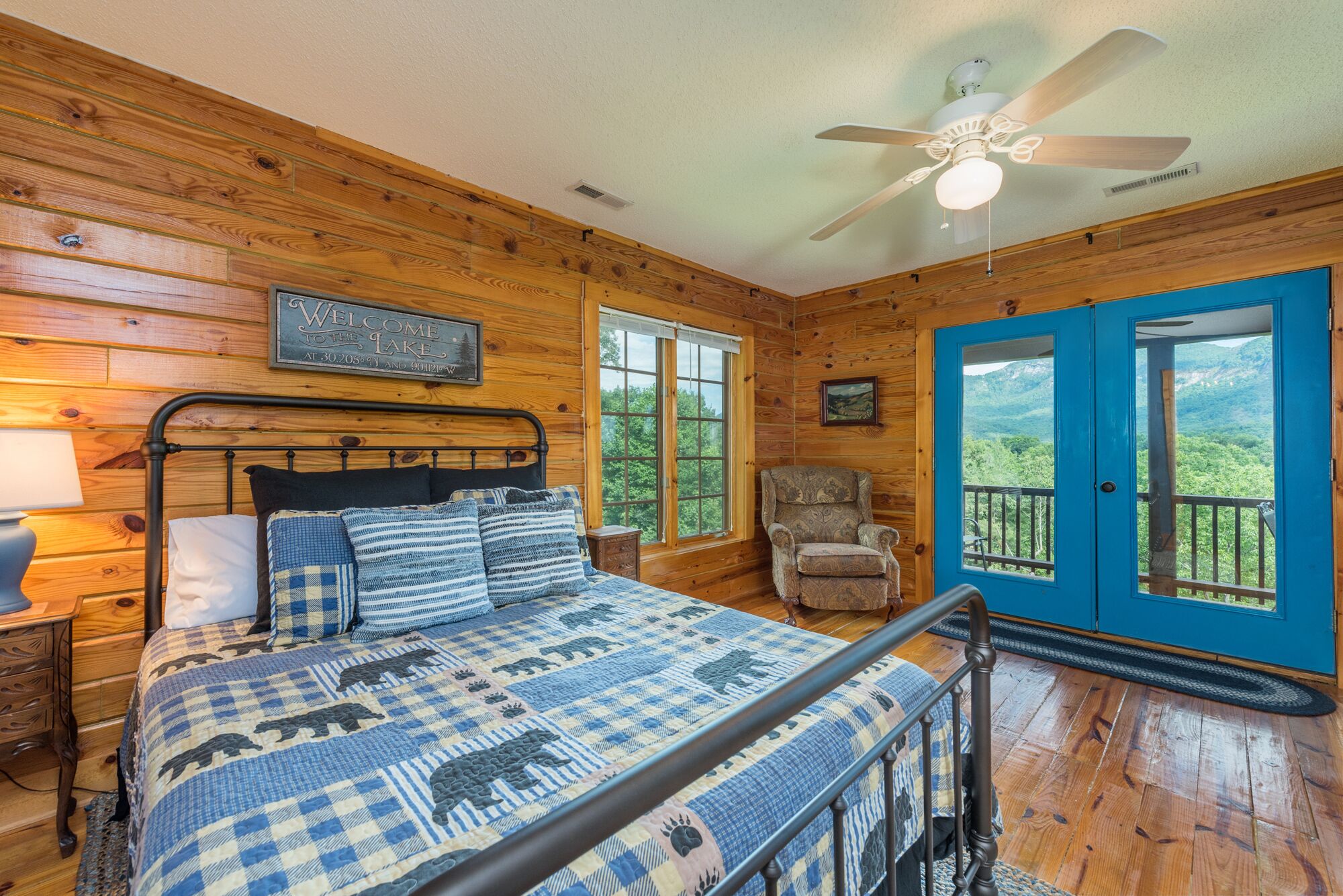 A wooden cabin room with a bed, a chair, a window, and a door leading to an outdoor balcony.