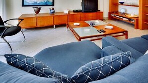 Een moderne woonkamer met een bank, salontafel, televisie, houten kast en kunstwerk aan de muur.