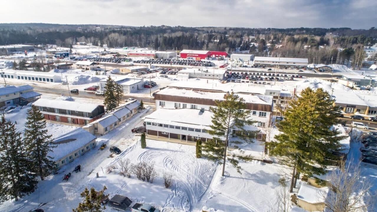 Luchtbeeld van een met sneeuw bedekt industriegebied met meerdere gebouwen, parkeerplaatsen en een groot, rood magazijn.