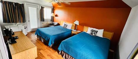 A hotel room with two beds, a desk, a chair, a ceiling fan, and a trash bin.