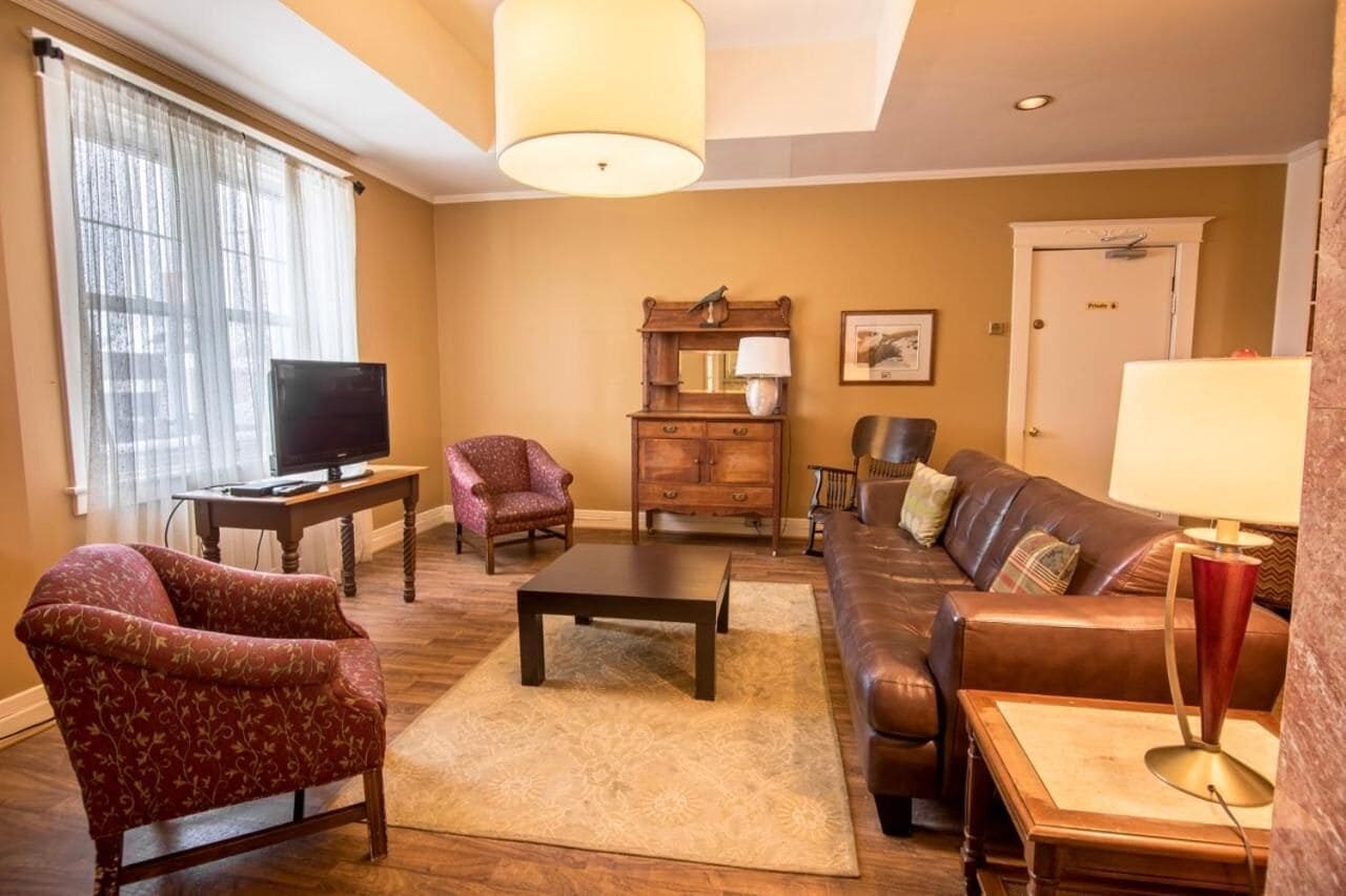 A living room with a brown leather sofa, a red patterned armchair, a wooden coffee table, a television on a stand, and a lamp on a side table.