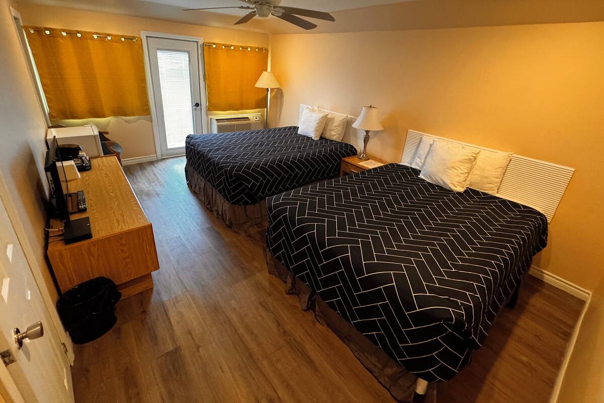 Een hotelkamer met twee bedden, een bureau, een plafondventilator en een badkamer met douchegordijn.