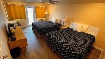 Een hotelkamer met twee bedden, een bureau, een plafondventilator en een badkamer met douchegordijn.