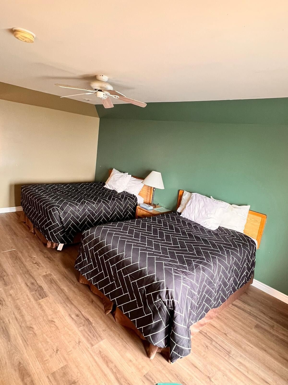 Una habitación con dos camas, un ventilador de techo y una pared verde.