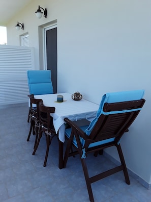 A patio with a table and four chairs, a small decorative item, and a door with a window. - Marianos Apartments (Kissamos)