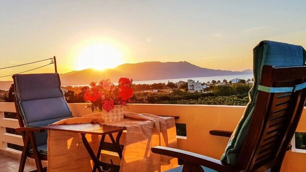 A balcony with two chairs, a table, and a vase of flowers. - Marianos Apartments (Kissamos)