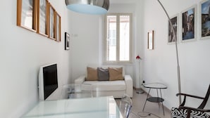 Un salon moderne avec une table à manger en verre, un canapé blanc agrémenté de coussins, un lampadaire et des tableaux encadrés accrochés au mur.
