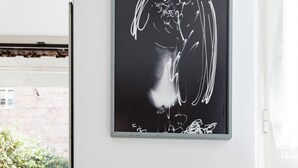 Une commode verte avec une tablette sur le dessus, une peinture abstraite en noir et blanc au-dessus, et des plantes en pot devant une fenêtre.
