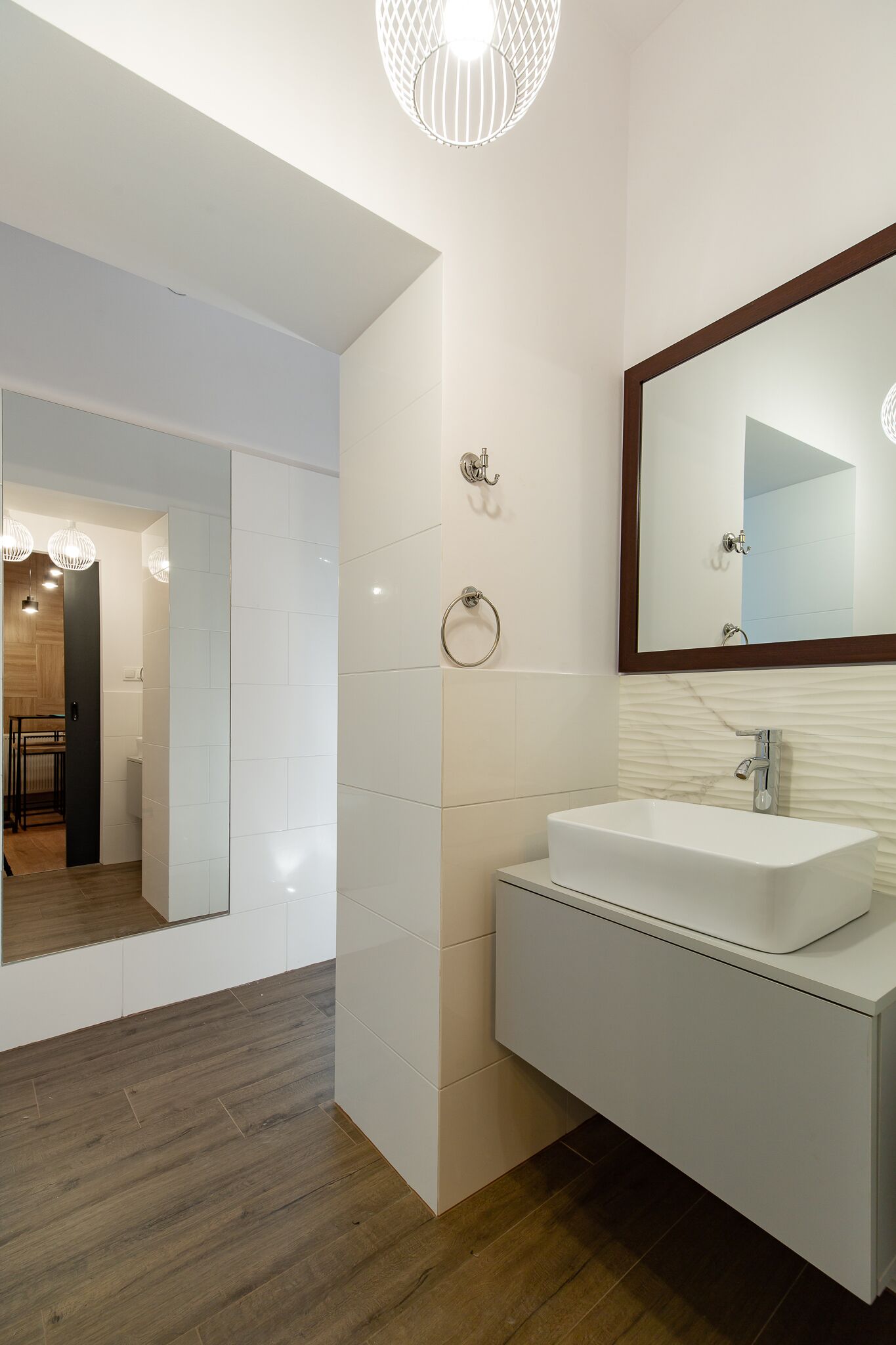 Un baño moderno con un tocador blanco, un espejo grande y suelo de madera.