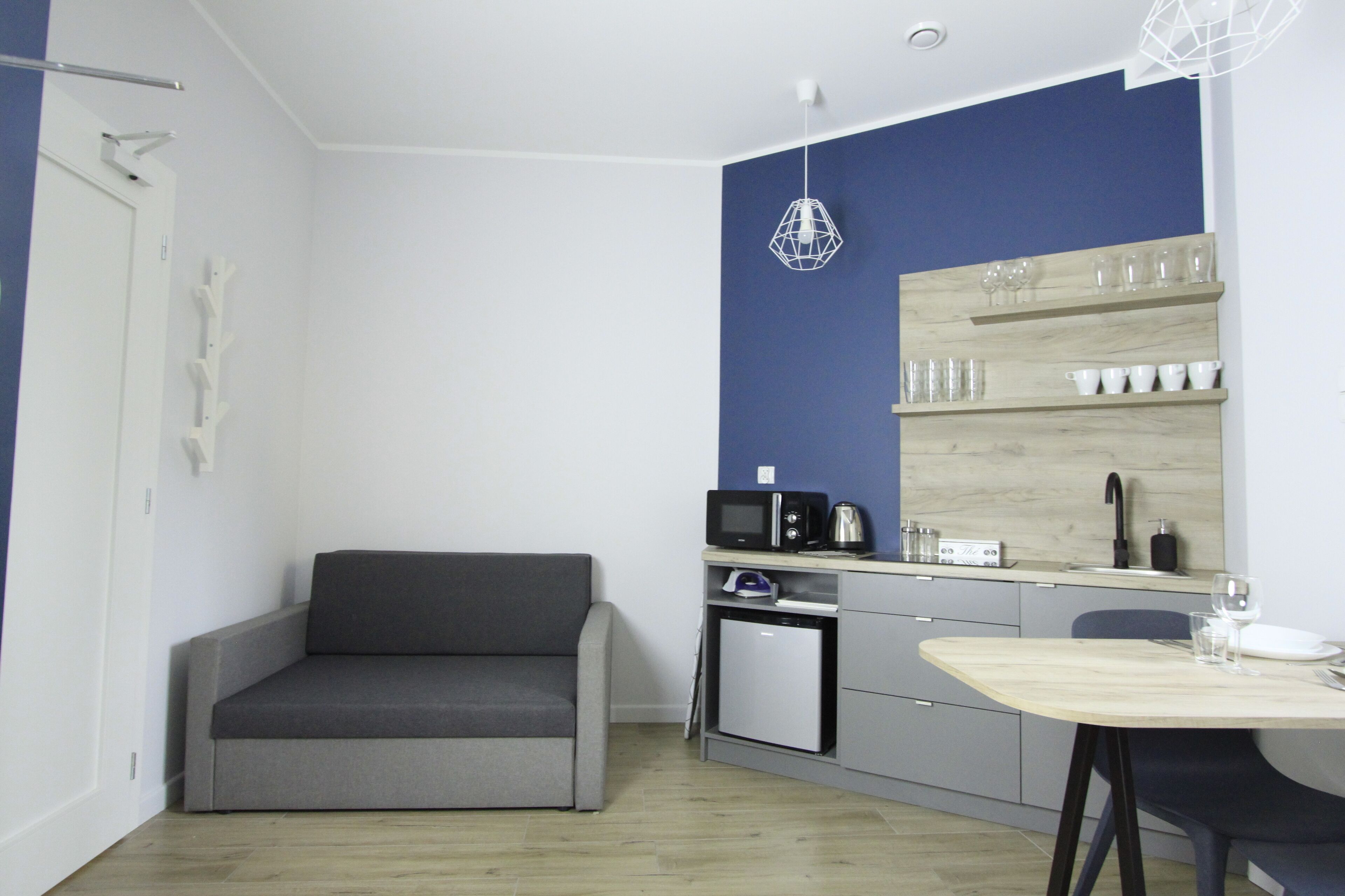 A compact kitchen with a microwave, toaster, and small refrigerator. There's a dining table with chairs and a sofa in the corner.
