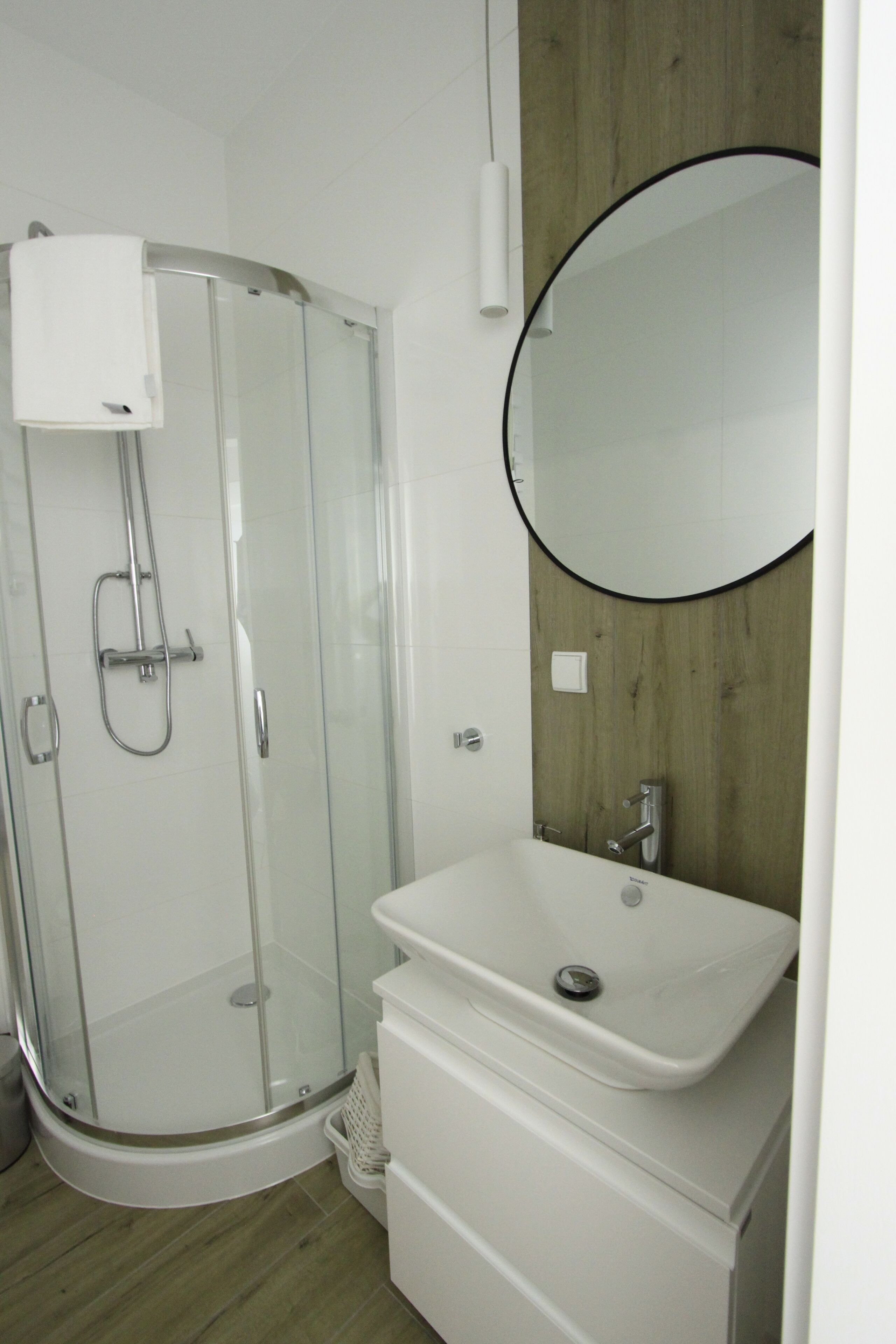 A modern bathroom with a glass-enclosed shower, a white sink, and a wooden accent wall.