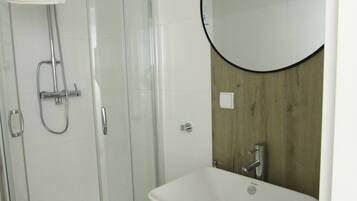 A modern bathroom with a glass-enclosed shower, a white sink, and a wooden accent wall.
