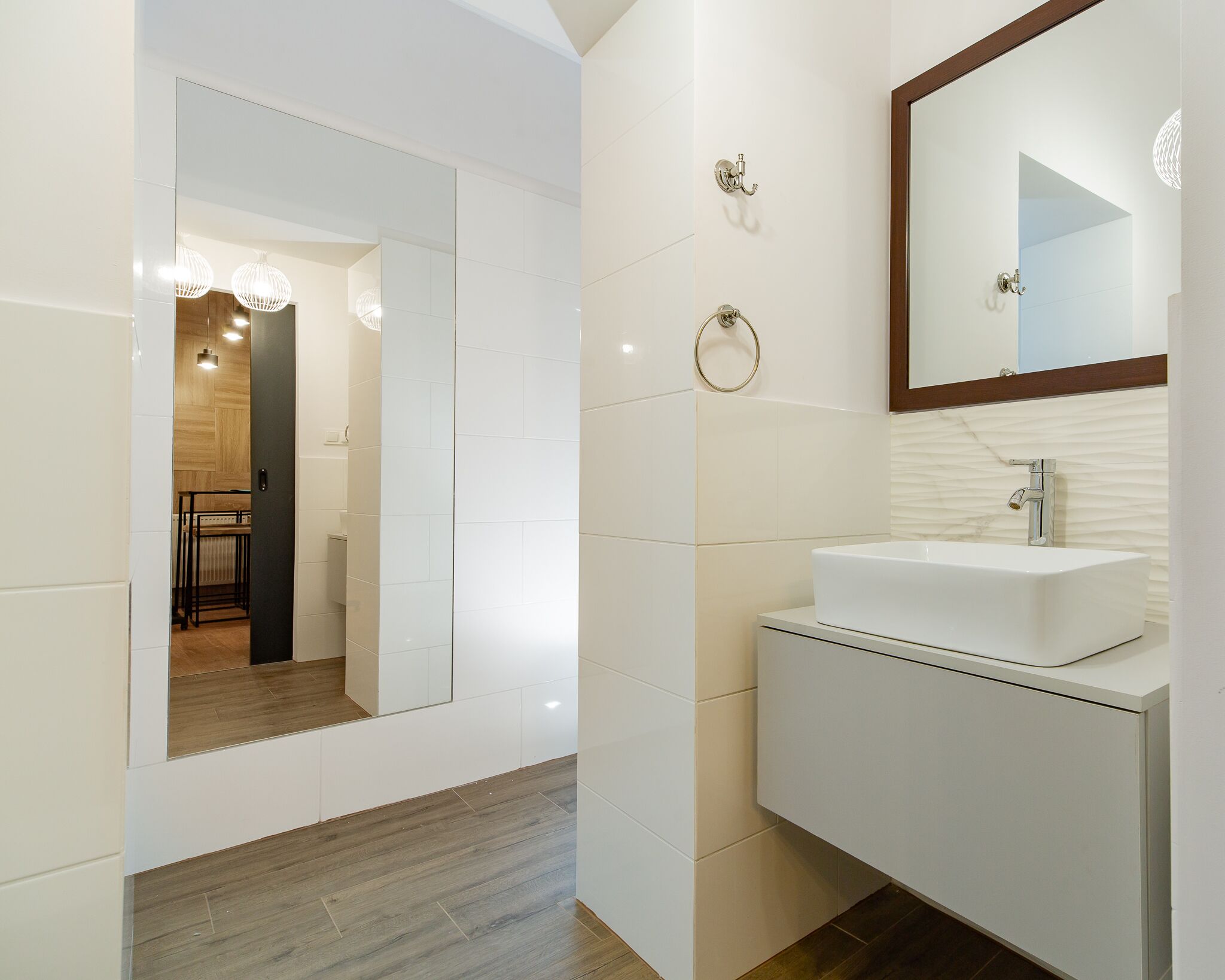 Un baño moderno con un tocador blanco, un espejo grande y suelo de madera.