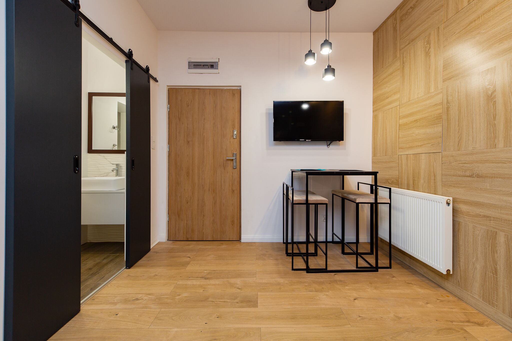 Ein modernes Zimmer mit Holzboden, einer Schiebetür, einem an der Wand montierten Fernseher und einer Heizung.