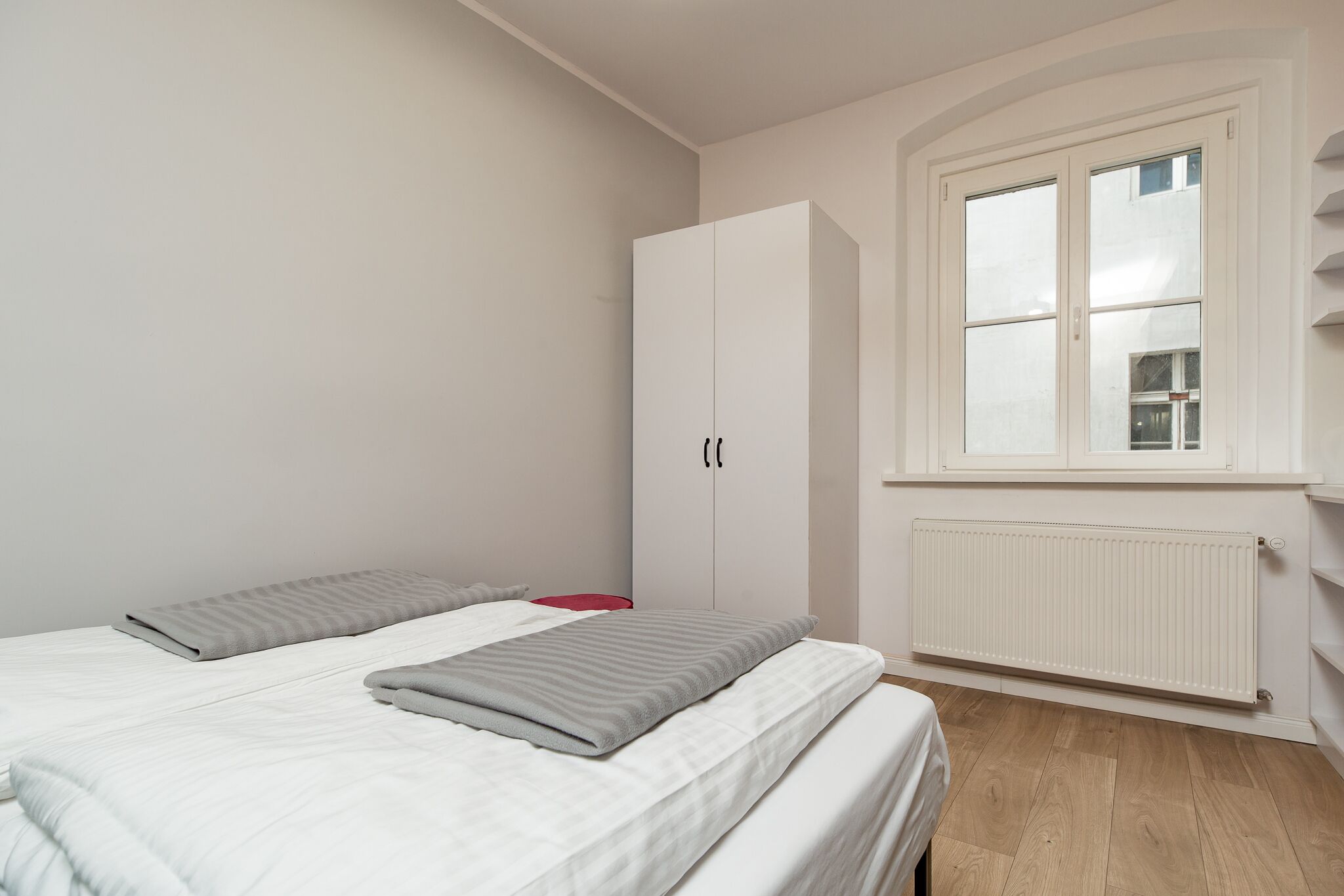 A bedroom with a bed, a wardrobe, a window, and a radiator.