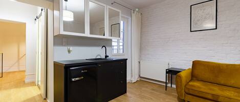 Un espacio habitable compacto con kitchenette, sofá y un cuadro en la pared.