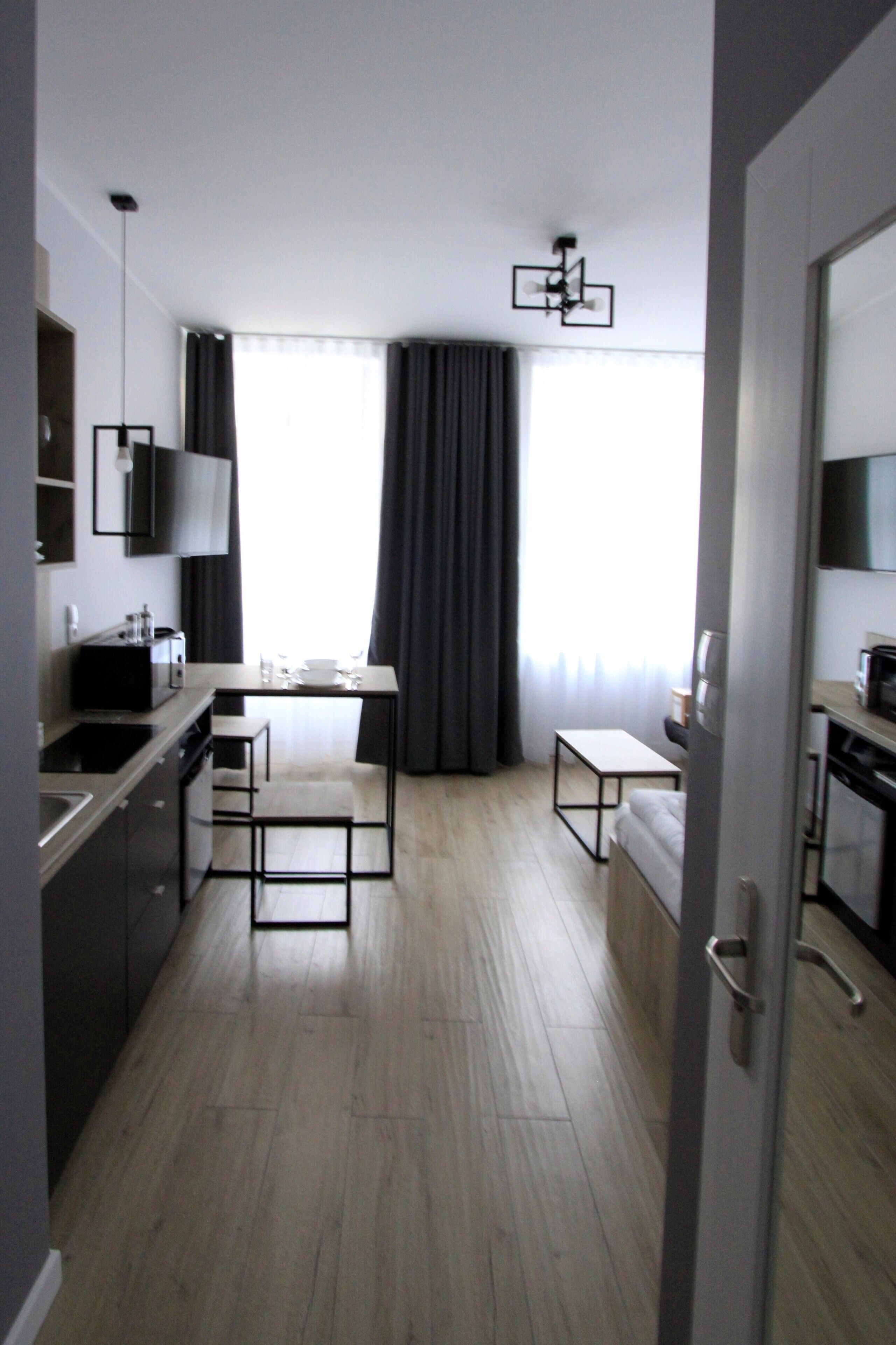 A modern hotel room with a kitchenette, a dining area, and a large window with curtains.