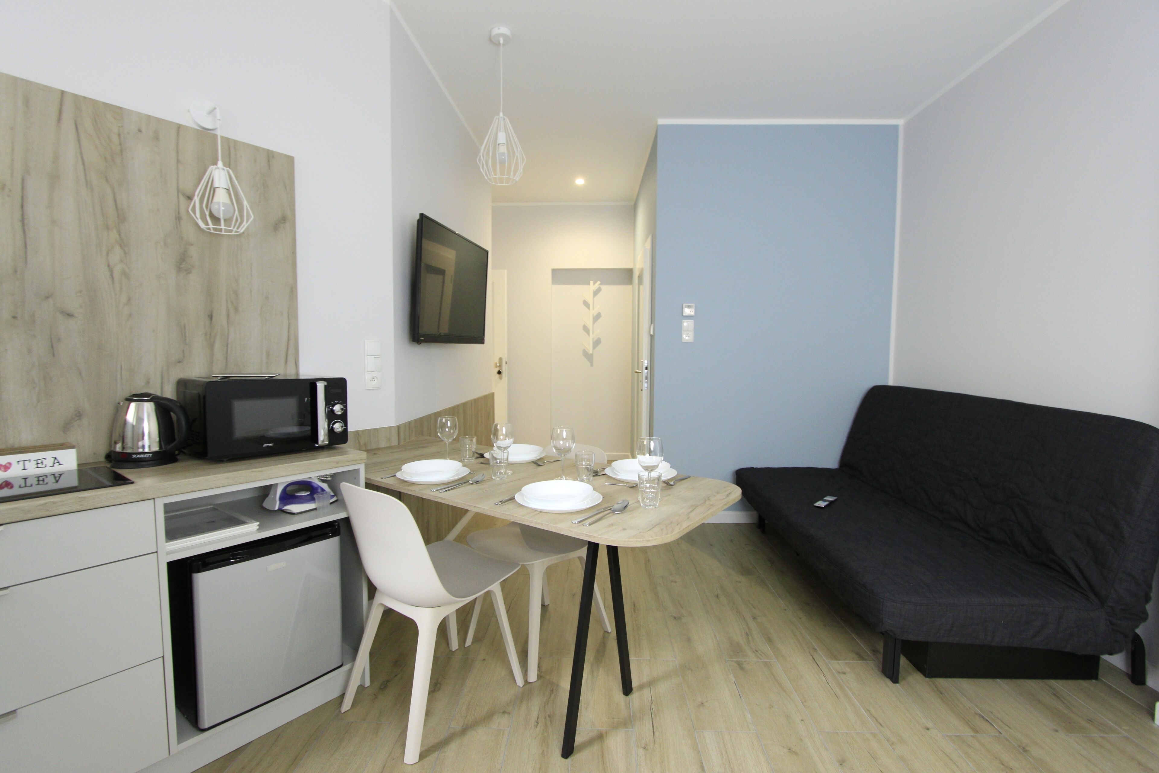 A compact living space with a kitchenette, dining table, and a black sofa.