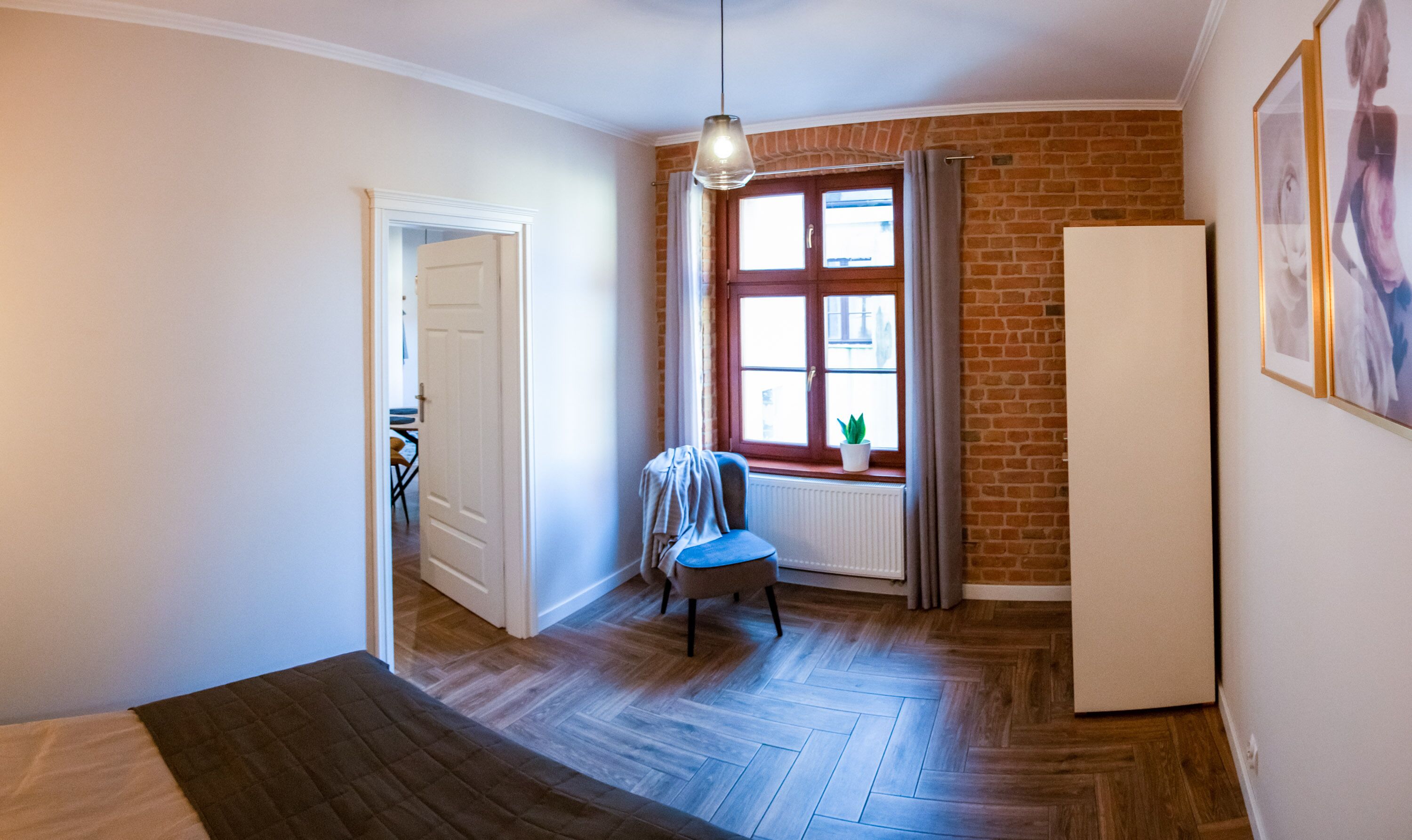 A room with a wooden herringbone floor, a white radiator, a blue chair, a white door, and a window with curtains.