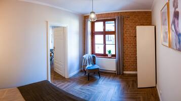 A room with a wooden herringbone floor, a white radiator, a blue chair, a white door, and a window with curtains.