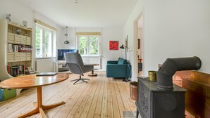 Un salon moderne avec un plancher en bois, une table ronde en bois, un fauteuil de bureau gris, un canapé turquoise et un poêle noir.