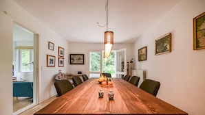 Une salle à manger avec une longue table en bois, des chaises et un luminaire suspendu.
