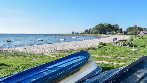 Une plage avec plusieurs bateaux, une rive sablonneuse et une rangée de maisons en arrière-plan.