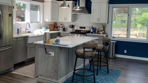 Una cocina moderna con una isla central, vigas de madera, armarios blancos y un ventanal grande.