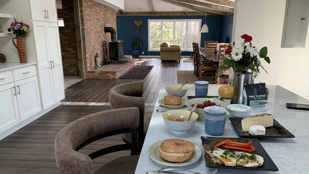 Una cocina moderna con zona de desayuno que incluye bagels, frutas, café y una fuente de quesos.