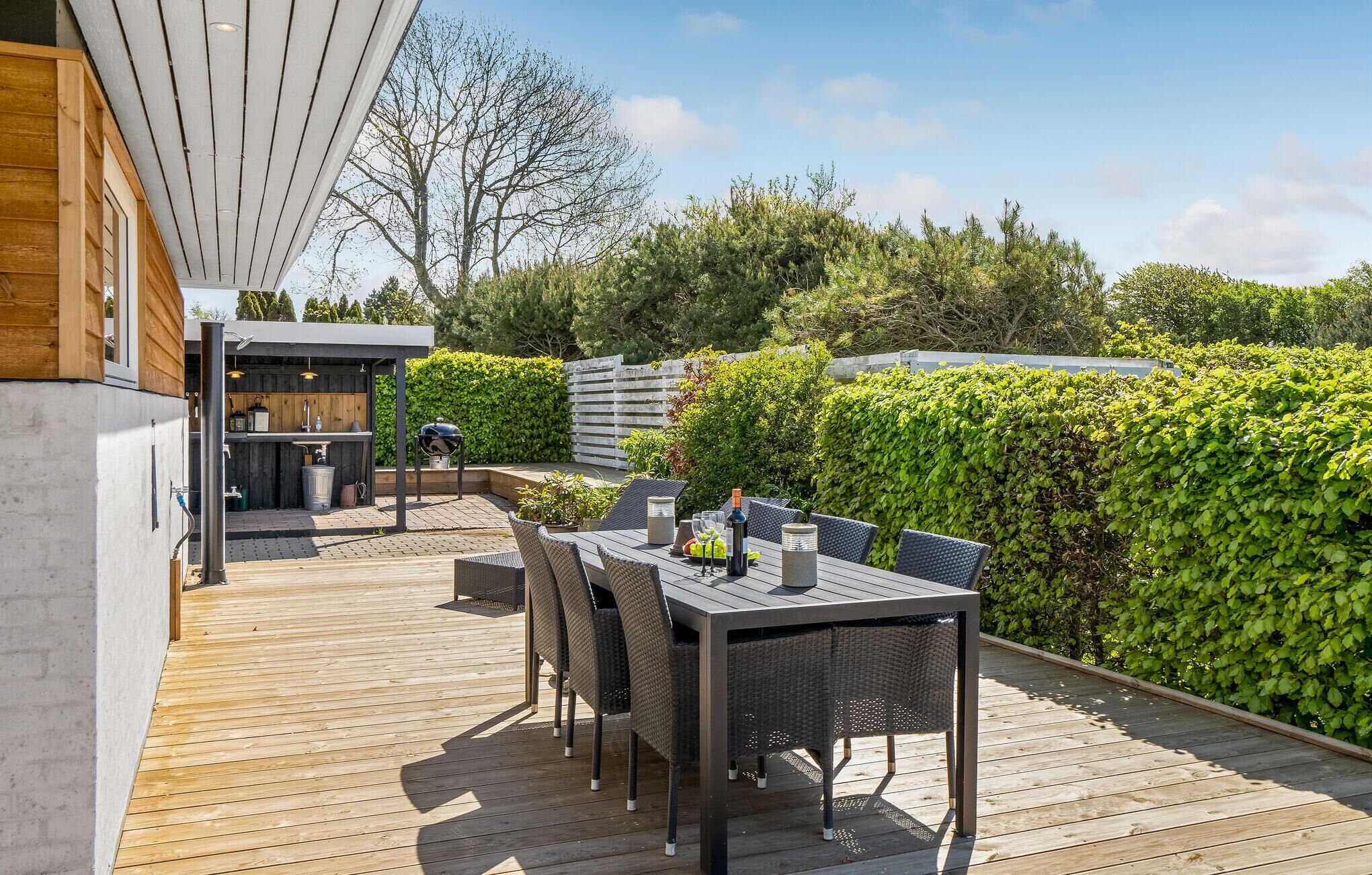 A wooden deck with a dining table and chairs, a barbecue grill, and a small kitchen area with a sink and counter.