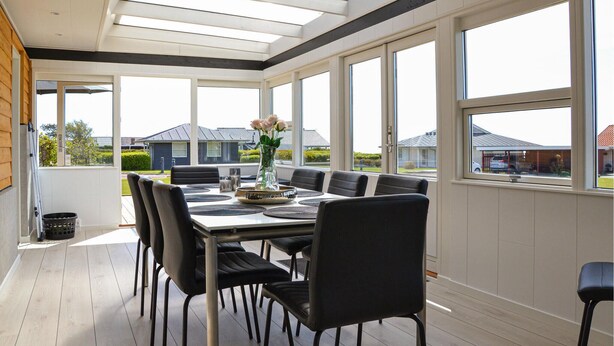 Un coin repas avec une table dressée pour six personnes, de grandes fenêtres et une vue sur les maisons à l’extérieur.