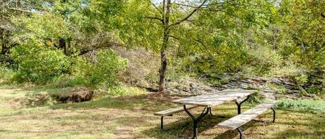 Una mesa de picnic en un área boscosa con césped y árboles.