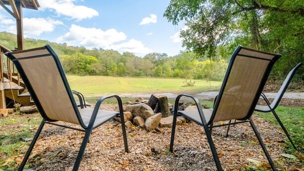 Two chairs facing a fire pit with a view of a grassy field and trees. - Cottage at the Creek ~ On S. Sylamore (Mountain View)