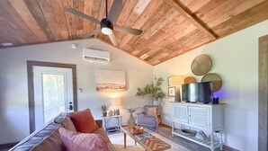 A living room with a sofa, coffee table, TV stand, and ceiling fan. - Cottage at the Creek ~ On S. Sylamore (Mountain View)