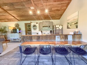 A kitchen with a central island, a dining area with chairs, and a wooden ceiling.