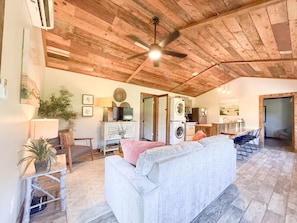 A spacious living area with a ceiling fan, a sofa, a television, and a kitchen area.
