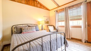 A bedroom with a bed, a nightstand, a chair, and a window with curtains. - Cottage at the Creek ~ On S. Sylamore (Mountain View)