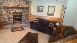 A stone fireplace, a dark brown sofa, a wooden coffee table, and a staircase with heart-shaped railings. - The Dairy at the Wegmueller Farm - stay on a Wisconsin farm! (Monroe)