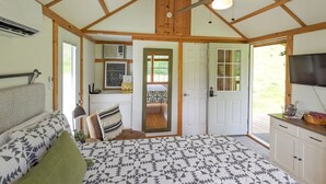 A bedroom with a bed, a desk, a chair, a ceiling fan, and a door leading to another room. - Cabin-ette at the Creek ~ a Tiny Ozark Getaway (Mountain View)