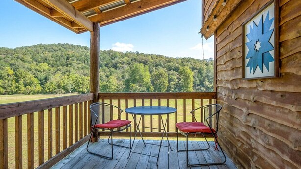A wooden deck with a table and two chairs, overlooking a forested landscape. - Cabin-ette at the Creek ~ a Tiny Ozark Getaway (Mountain View)