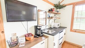A compact kitchen with a flat-screen TV, coffee maker, microwave, and a wooden countertop. - Cabin-ette at the Creek ~ a Tiny Ozark Getaway (Mountain View)